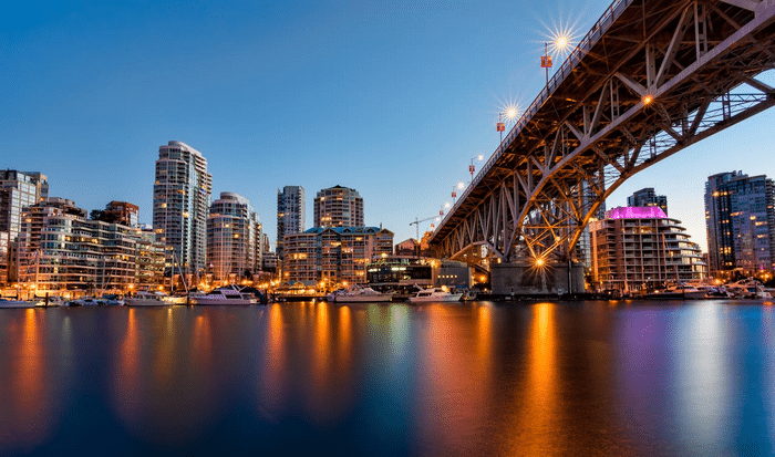 A panoramic view of city buildings across the river and the bridge above