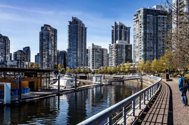 A photo of city buildings in the distance with water being on the left behind the fence